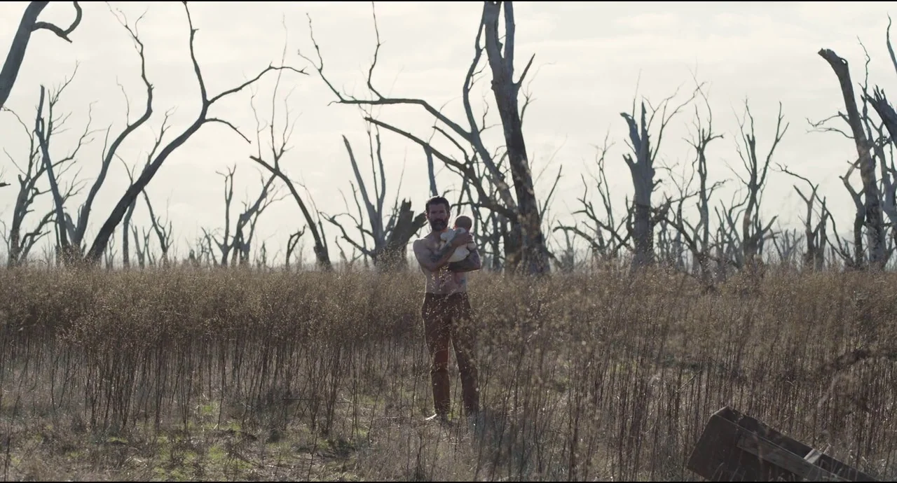 True History of the Kelly Gang (2019) movie still: fullbody — A field filled with dead, leafless trees under a pale sky. A shirtless man stands in…