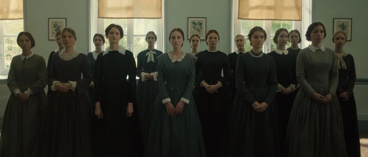A Quiet Passion (2016) movie still: fullbody — A group of women in 19th-century attire stands in a room with white walls. They face the camera in…