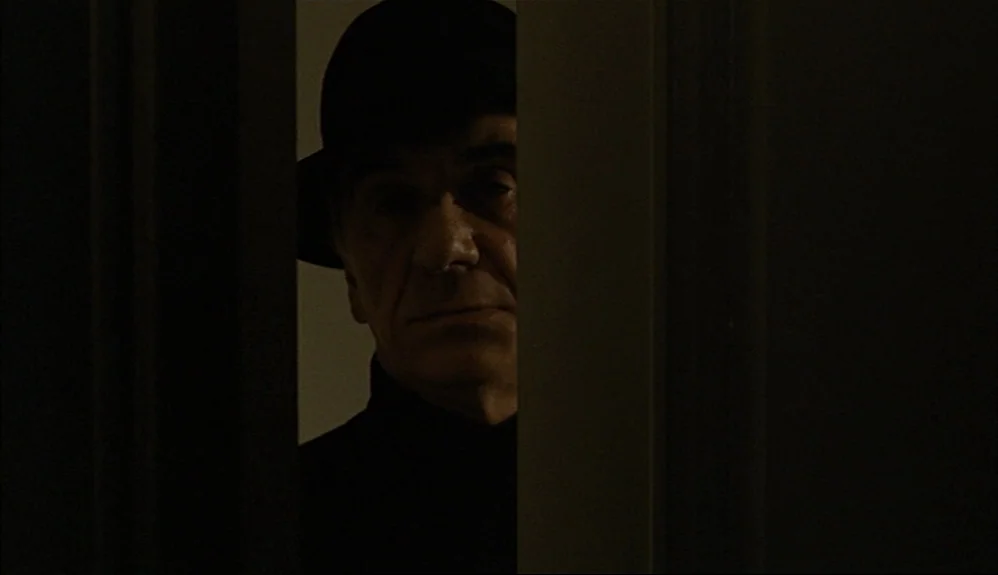 The Godfather Part II (1974) movie still: closeup — A dark indoor space is divided by a vertical door frame and thick shadow. An older man wearing a…
