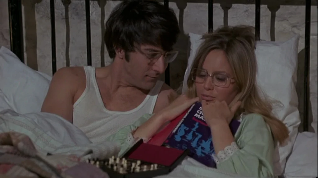 Straw Dogs (1971) movie still: medium — A man and a woman rest in a bed with a metal headboard. The woman holds a book against her chest while a…