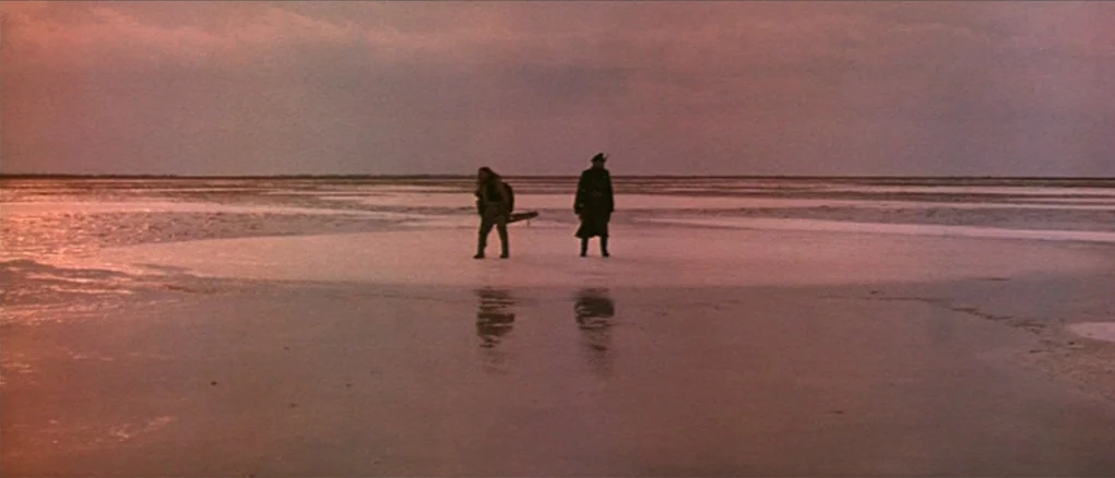 Dersu Uzala (1975) movie still: wide — A vast, barren salt flat stretches toward a distant, hazy horizon under a sunset sky. Two men stand…