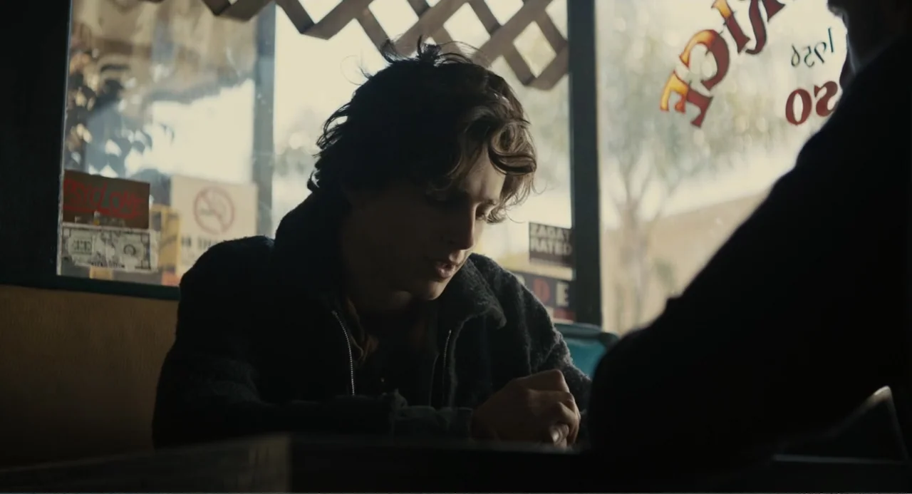Beautiful Boy (2011) movie still: medium — A man sits inside a booth at a diner with a window behind him. He leans forward with his hands clasped…