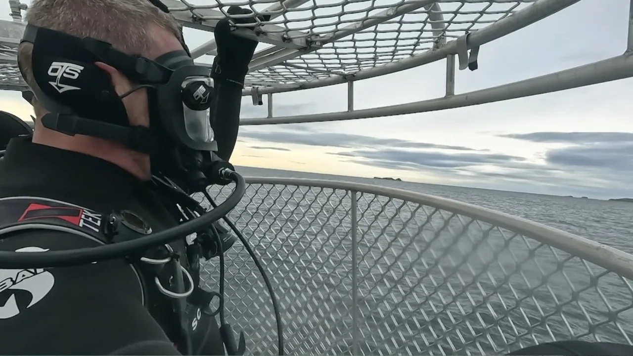Air Jaws: Final Frontier (2023) movie still: medium — A metal shark cage floats on an open sea under an overcast sky. A diver wearing a full-face…
