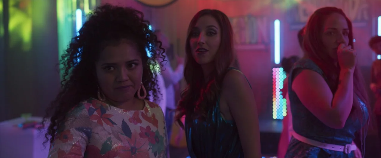 Crazy for Change (2020) movie still: medium — A dimly lit interior nightclub features colorful neon wall accents and blurred background figures.…