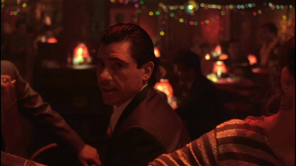 Goodfellas (1990) movie still: medium — A dark, crowded nightclub features blurred colorful bokeh lights in the background. A man in a dark suit…