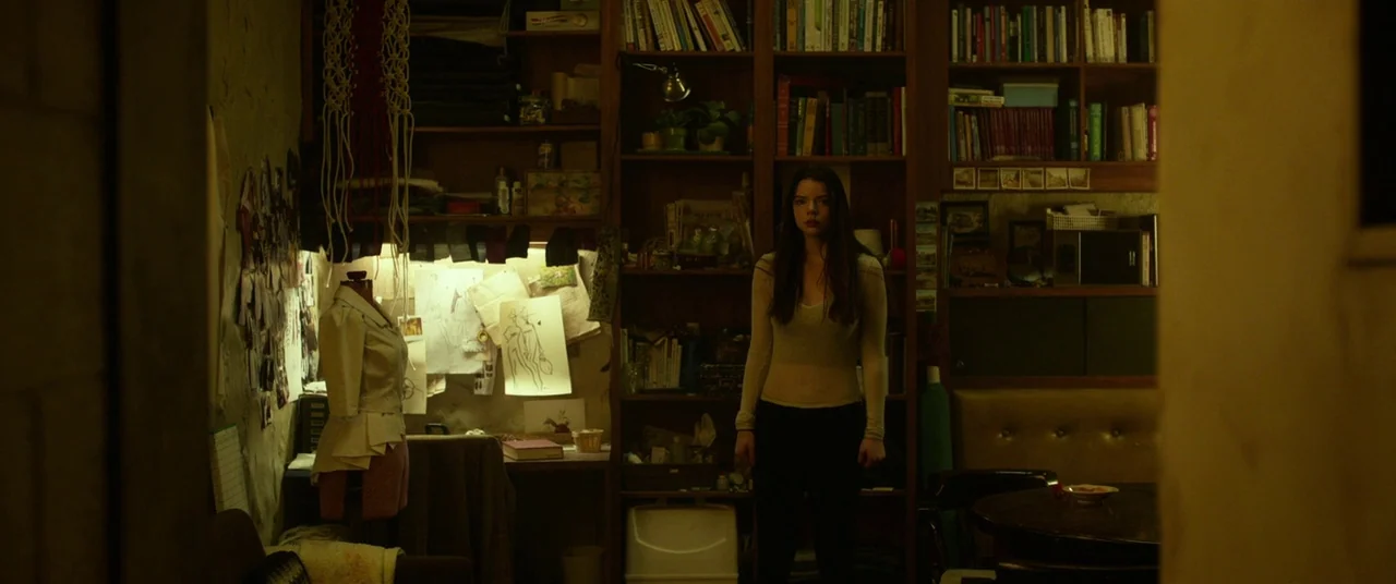 Split (2016) movie still: fullbody — A cluttered apartment workshop features tall bookshelves and a sewing mannequin on the left. A young woman…