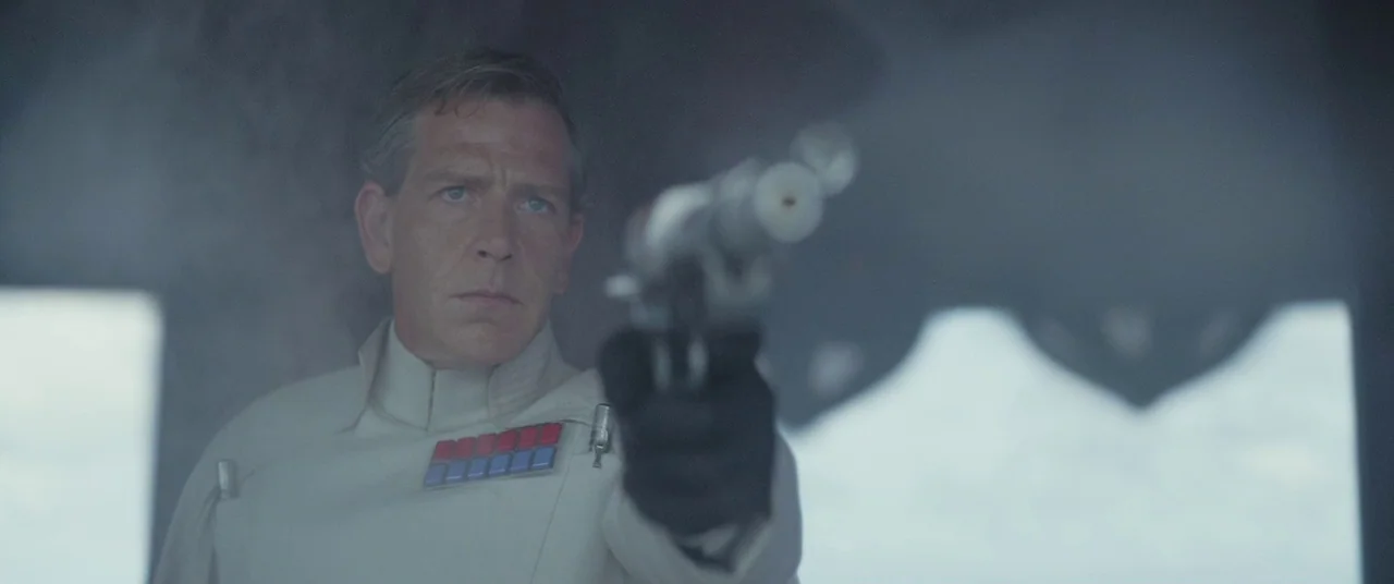 Rogue One: A Star Wars Story (2016) movie still: medium — A man in a stark white military uniform stands against a hazy backdrop. He aims a silver…