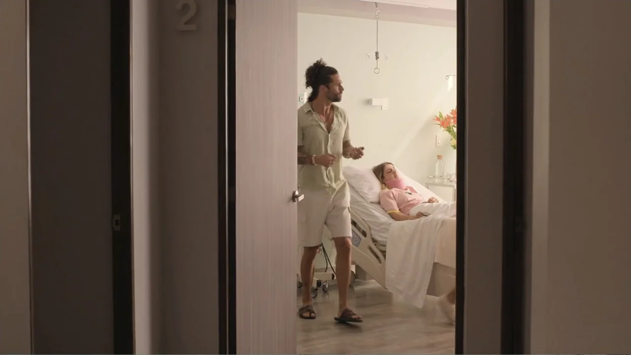Double Pregnant 2 (2022) movie still: fullbody — A clean hospital room contains a hospital bed and a man standing near the door. A woman rests in…