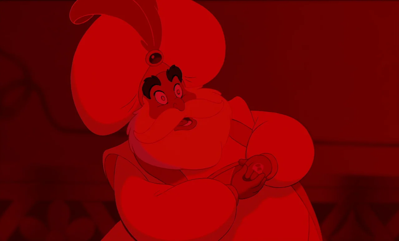 Aladdin (1992) movie still: medium — An older man wearing a turban stands in a dimly lit, monochromatic red room. He gazes upward with a wide-eyed…