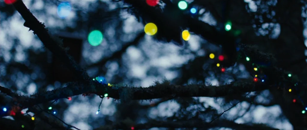 The Hunter (2011) movie still: wide — Dark tree branches covered in lichen are wrapped in multicolored festive string lights at night. The lights…