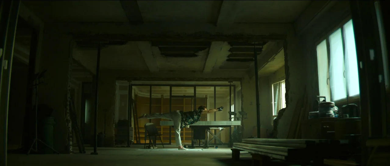 The Killer (2023) movie still: wide — An unfinished industrial space features exposed concrete ceilings and large windows letting in daylight. A…