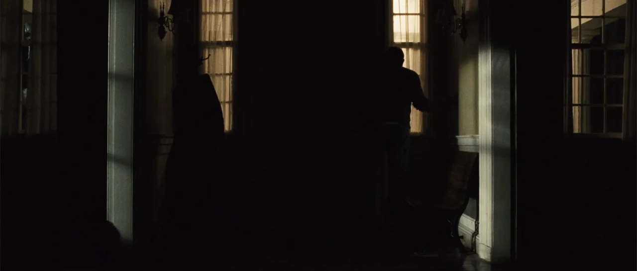 The New Daughter (2009) movie still: wide — A dimly lit interior hallway features tall windows with sheer curtains along the walls. Two silhouetted…