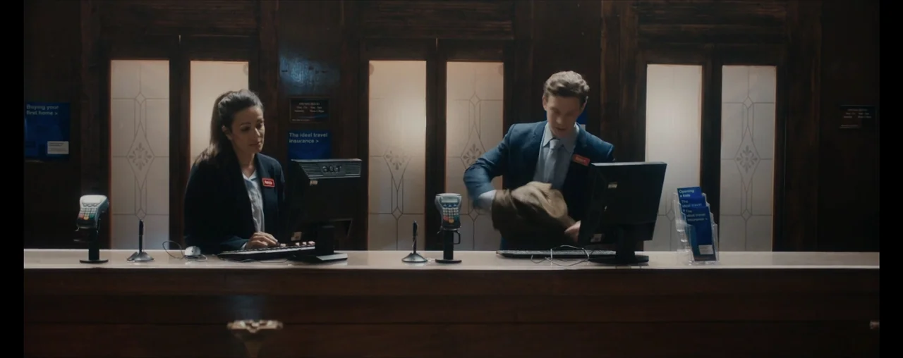 The Wrong Tenant (2022) movie still: medium — An interior counter features wood paneling and multiple computer monitors at workstations. A woman and…