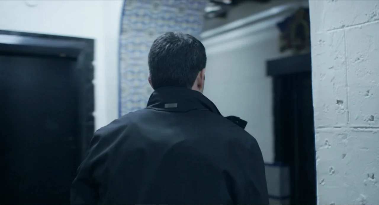 Instantes Capturados (2022) movie still: medium — An interior hallway features white-painted block walls and a dark arched threshold. A man wearing…