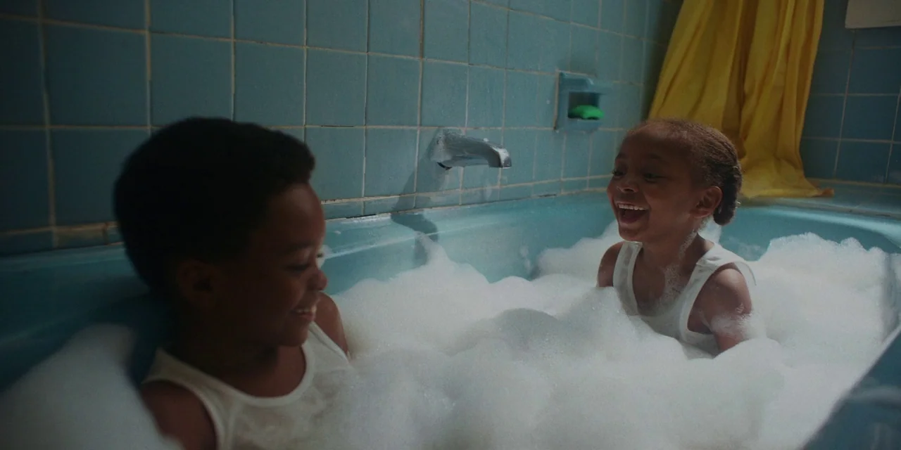 If Beale Street Could Talk (2018) movie still: medium — A bathroom features blue square tiles and a yellow curtain hanging on the side. Two children…