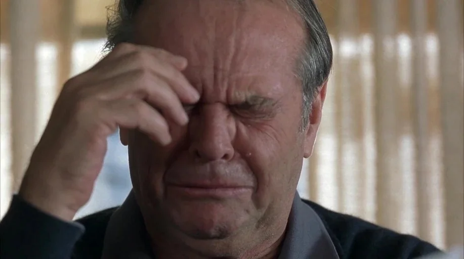 About Schmidt movie still: closeup — A man stands indoors in front of window curtains that filter soft natural light. He brings his right hand up to…