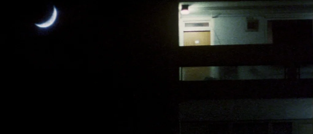 Wonderland (1999) movie still: establishing — A dark night exterior view showing the exterior of a multi-story residential apartment complex. A…