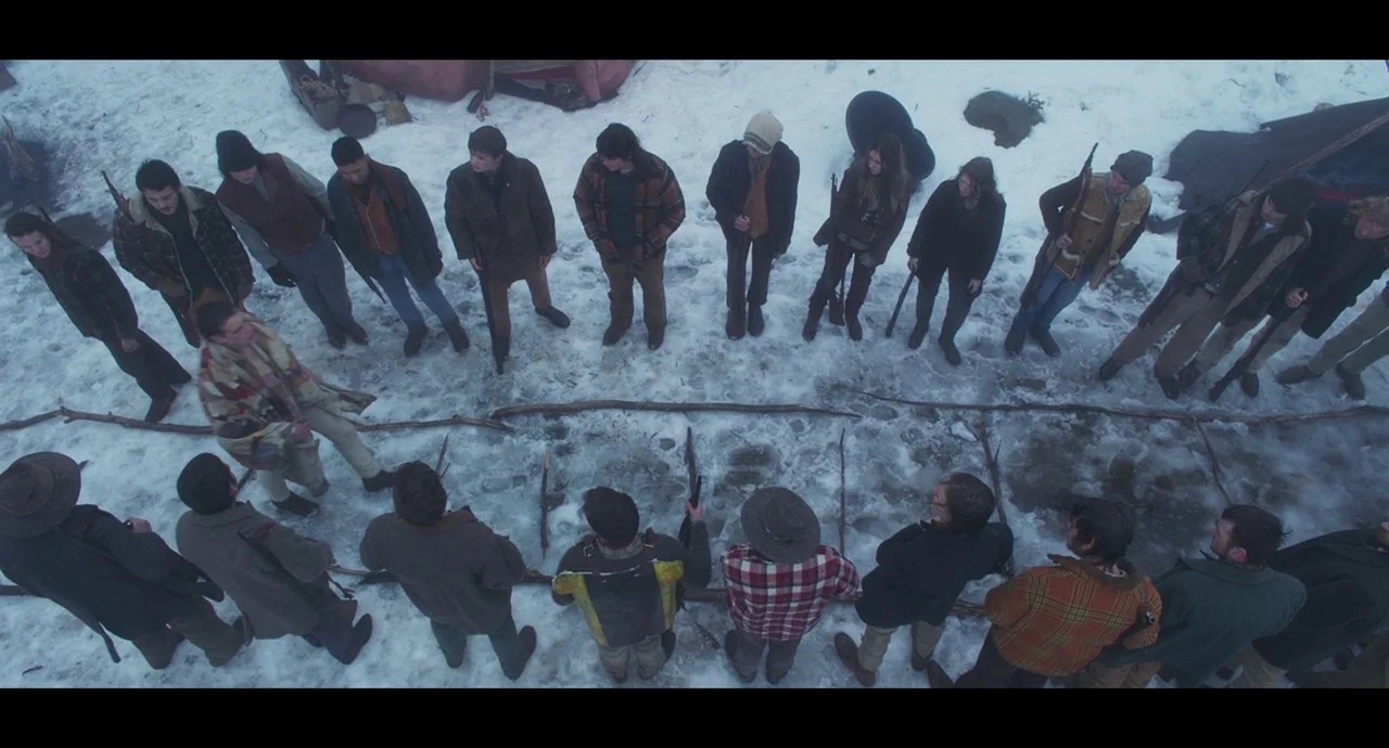 True History of the Kelly Gang (2019) movie still: wide — A group of people stands in a wide circle on a snow-covered ground. A man in a patchwork…