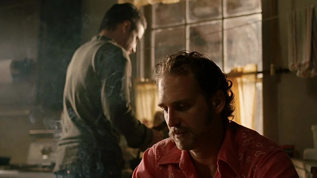 Undertow (2004) movie still: medium — A residential room featuring a window with yellow curtains and a stove in background. One man sits in the…