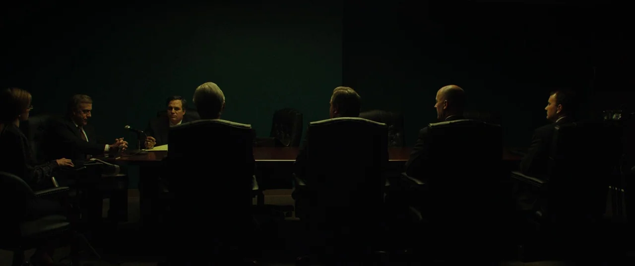 Dark Waters (2019) movie still: wide — A dimly lit conference room features a long dark table surrounded by business professionals. Several men and…