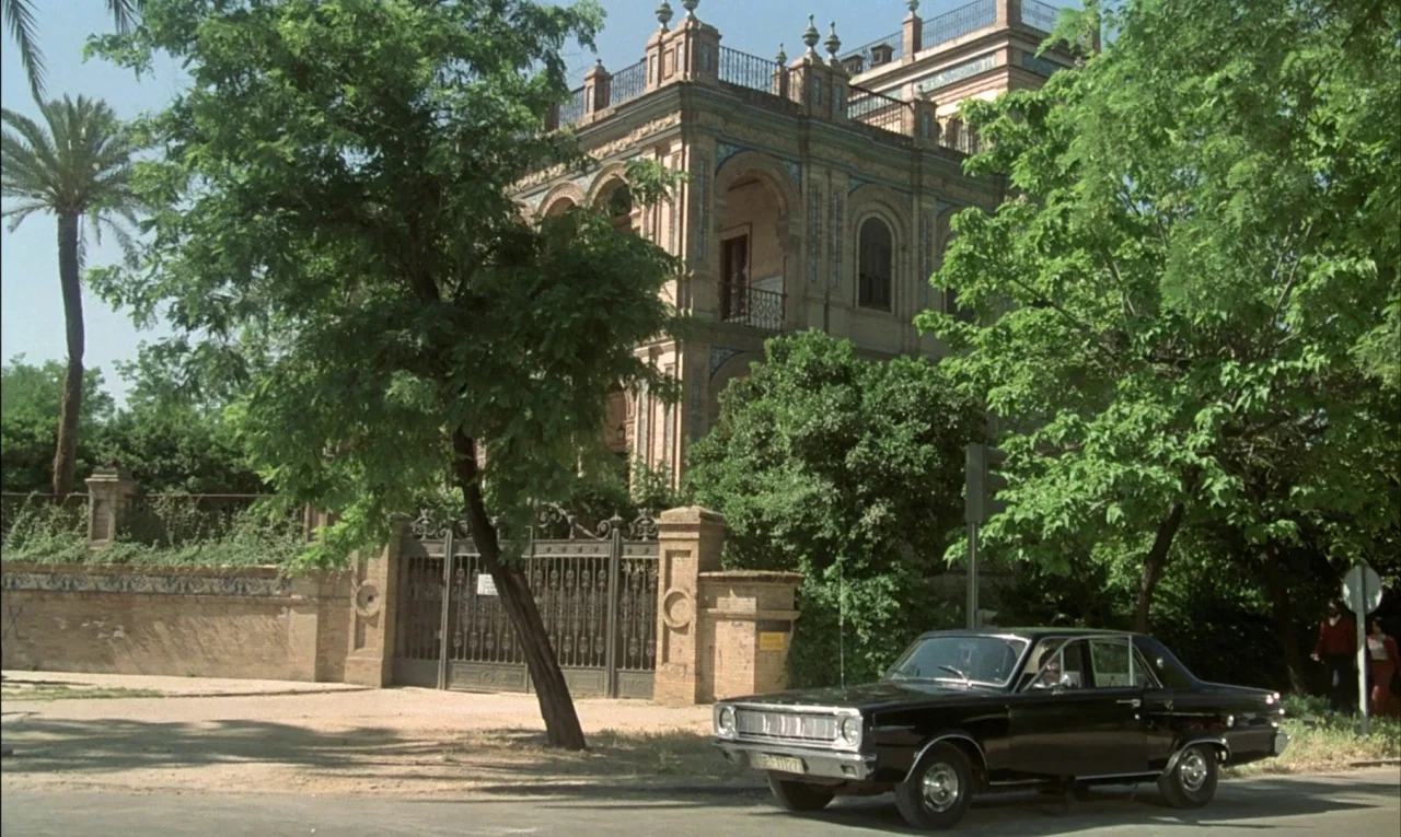 That Obscure Object of Desire (1977) movie still: wide — A historic yellow-brick villa with intricate tile work stands behind a gated wall. A black…