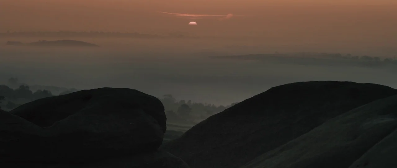 Sightseers (2012) movie still: establishing — A misty, expansive landscape features large dark rock formations in the foreground silhouette. The sun…