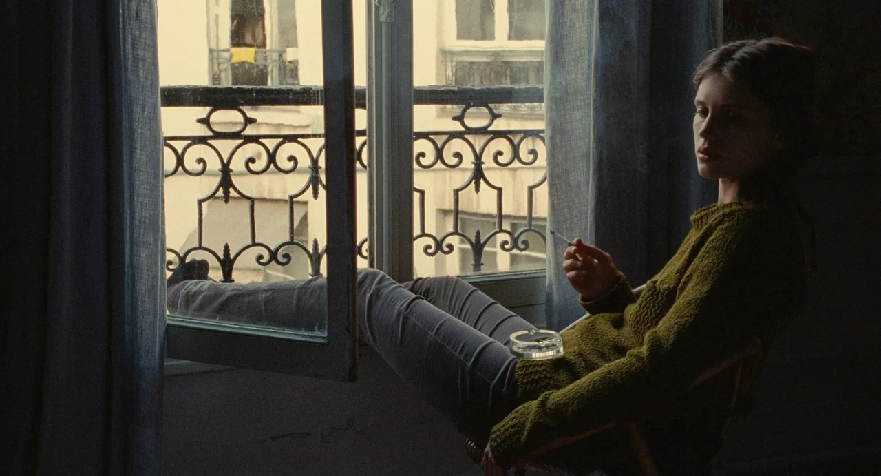 Young & Beautiful (2013) movie still: medium — A woman sits in a chair by a window with wrought iron balcony railing. She holds a cigarette while…