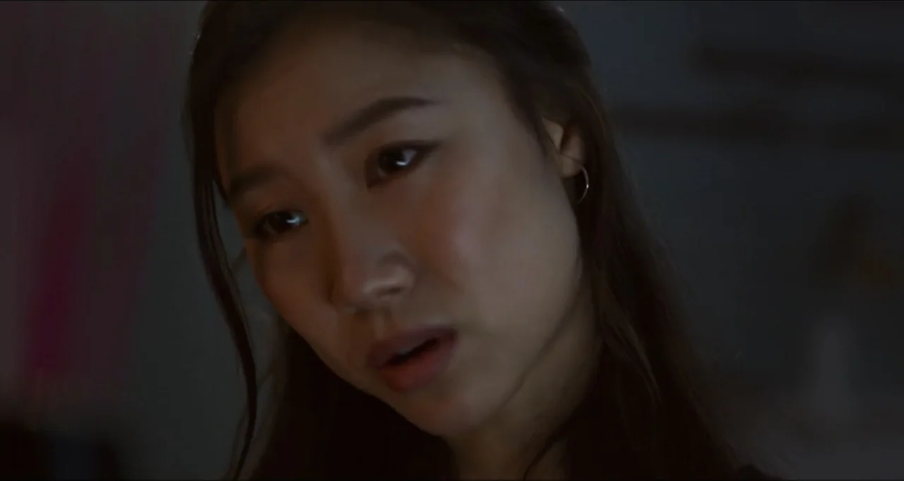 Five Blind Dates (2024) movie still: closeup — A dimly lit interior room at night provides a dark, neutral backdrop. An East Asian woman with long…