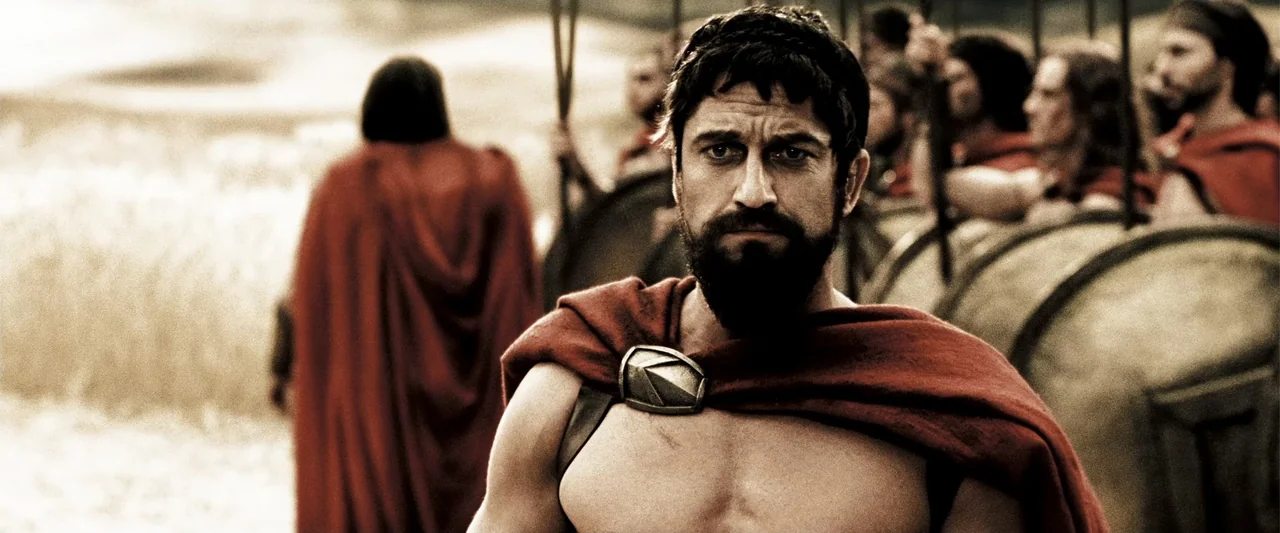 300 (2007) movie still: medium — A group of Spartan soldiers stands on an open terrain during a military engagement. A muscular bearded man in a red…