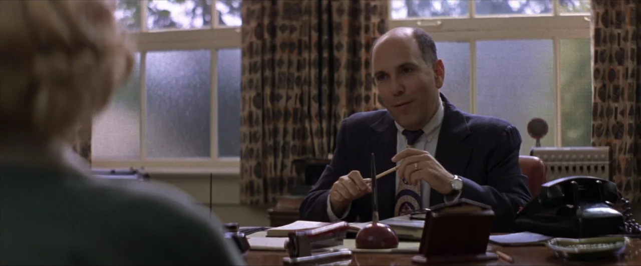 This Boy's Life (1993) movie still: medium — A 1960s office features wooden furniture, a rotary telephone, and patterned curtains by the window. A…