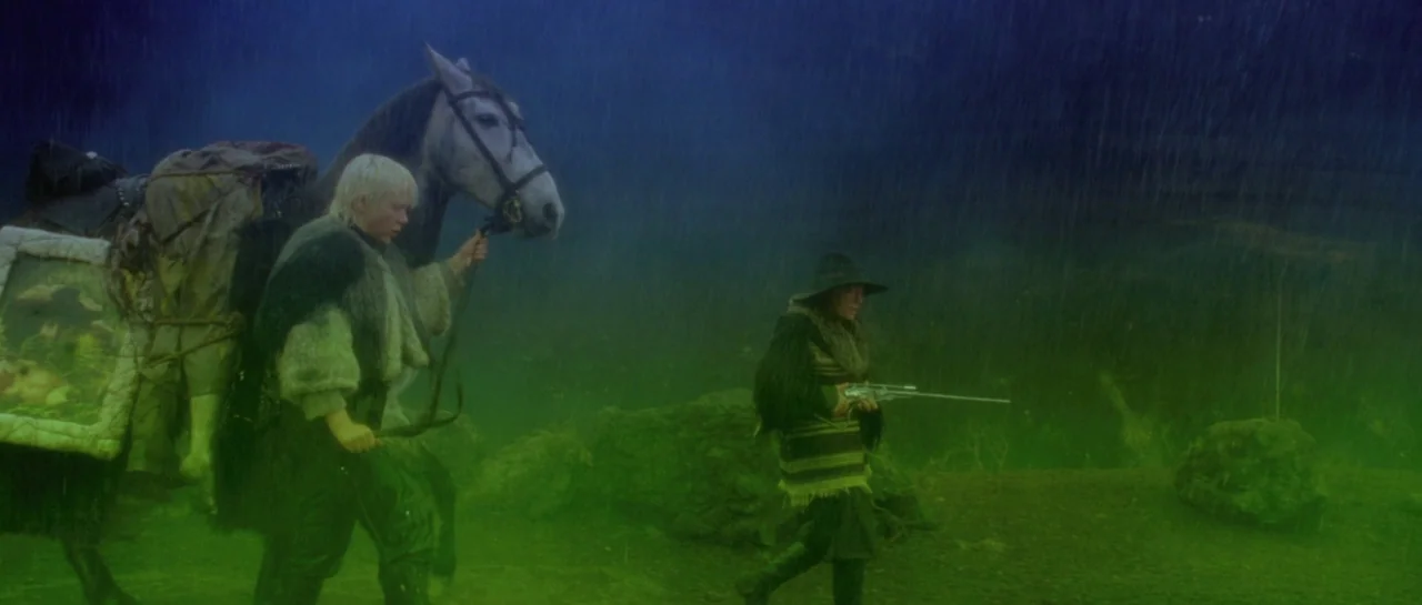 After Blue (2021) movie still: wide — A pair of travelers move across a misty landscape under heavy rainfall. The person leads a saddled horse…