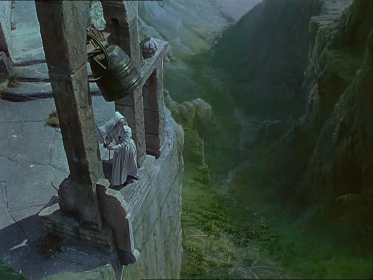 Black Narcissus (1947) movie still: wide — A stone bell tower sits precariously on the edge of a deep mountain gorge. A woman in a white nun's habit…