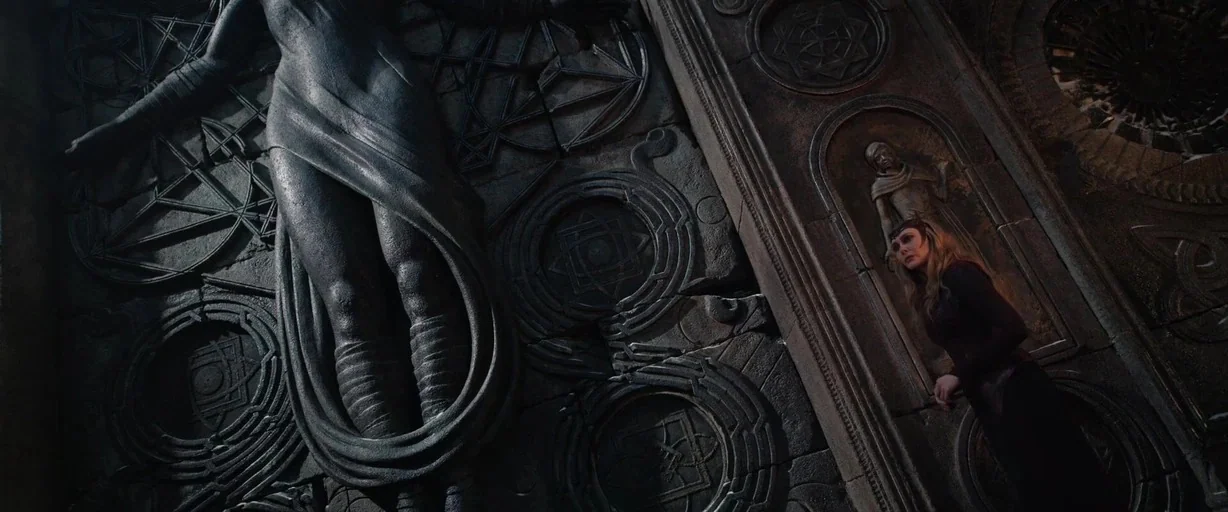 Doctor Strange in the Multiverse of Madness (2022) movie still: wide — A dark, ancient stone wall features massive bas-relief carvings of esoteric…