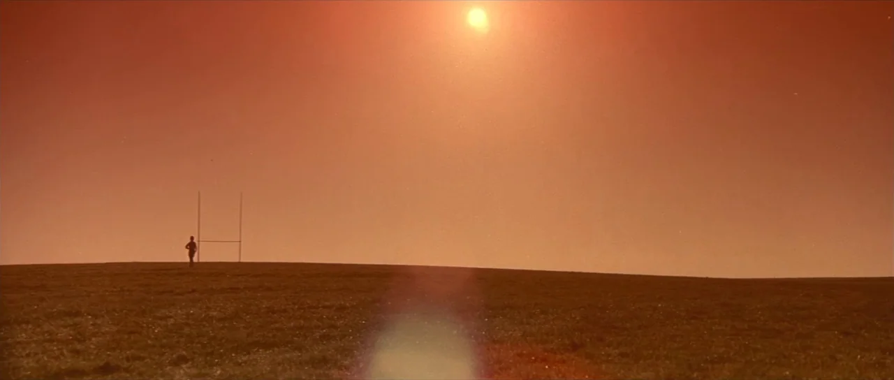 Pink Floyd The Wall (1982) movie still: wide — A flat, grassy field extends to a horizon line under a bright orange sky. A single rugby goal post…