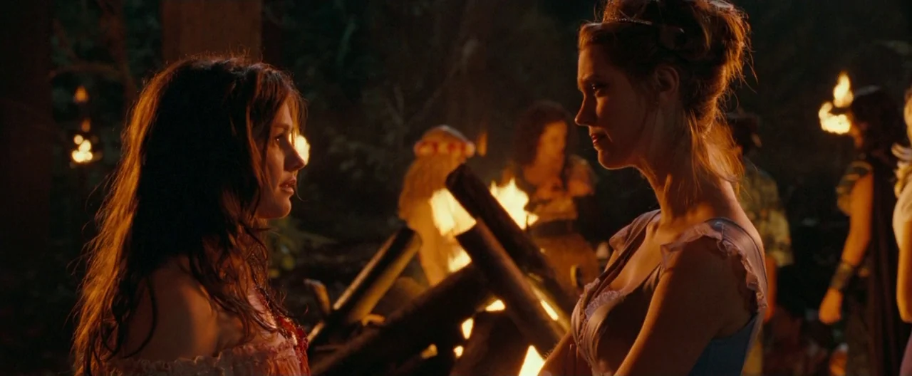 Trick ‘R Treat (2007) movie still: medium — An outdoor night setting illuminated by a bright roaring campfire in the woods. Two young women stand in…