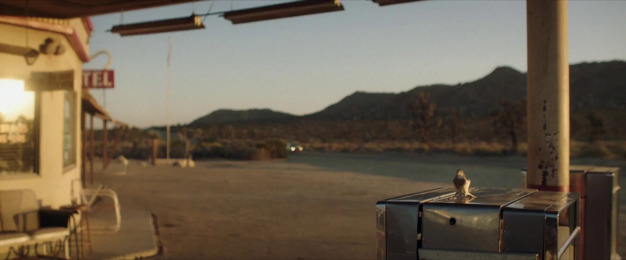 The Last Stop in Yuma County (2023) movie still: wide — An arid desert roadside fuel station at golden hour with distant mountains visible. A small…
