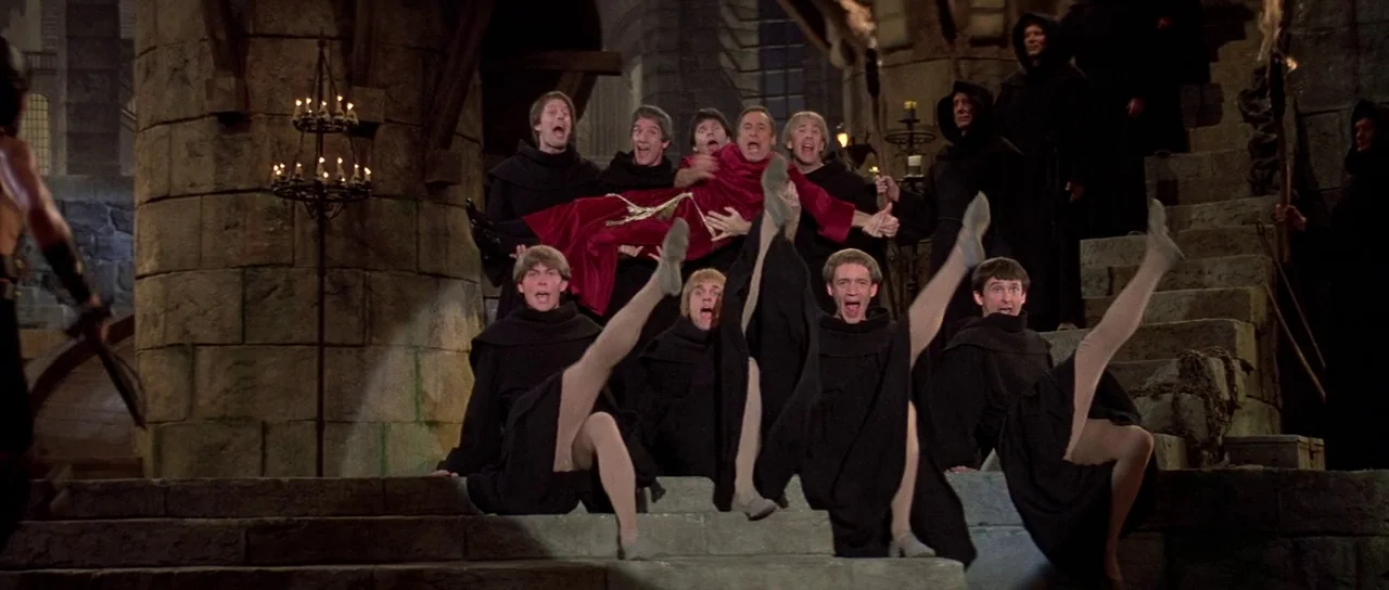 History of the World: Part 1 (1981) movie still: wide — A dark stone castle interior features a group of monks gathered on steps. Several monks…