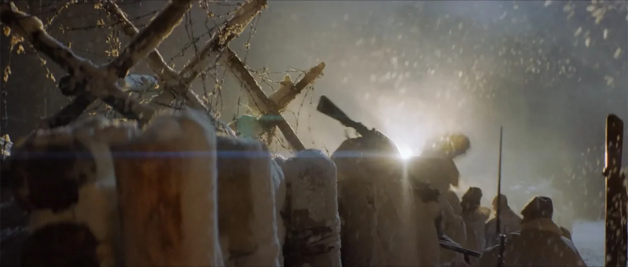The Rifleman (2019) movie still: wide — A snowy, darkened battlefield trench features wooden reinforcements and barbed wire barricades. Several…