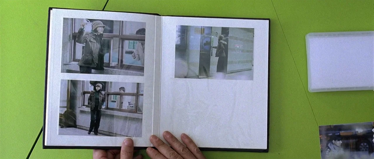 Lady Vengeance (2005) movie still: medium — A top-down view of a photo album lying flat on a bright lime-green table. The album contains several…