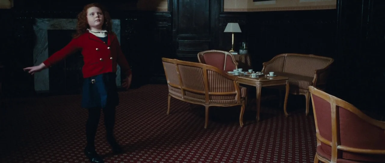 Our Day Will Come (2010) movie still: fullbody — A dimly lit room with dark wood paneling, ornate furniture, and a patterned red carpet. A young…