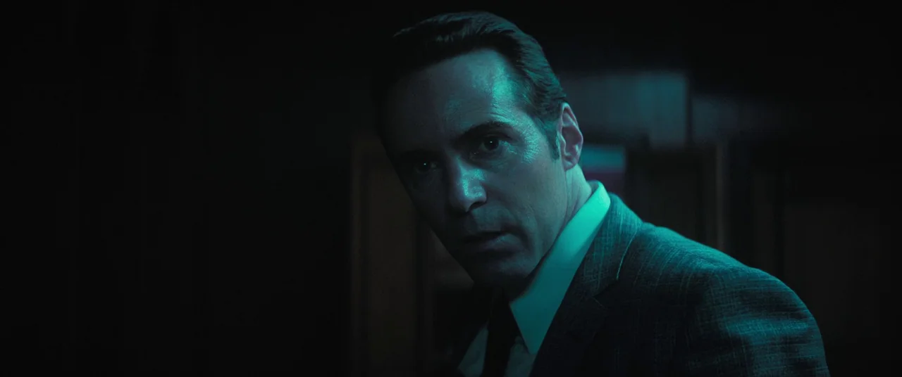 The Many Saints of Newark (2021) movie still: closeup — A dark indoor space is illuminated by an artificial blue-green light source. A man in a suit…