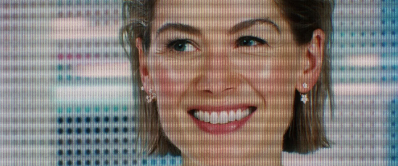 I Care A Lot (2020) movie still: closeup — A close-up view of a digital monitor displaying a video feed. A woman with short hair smiles directly…