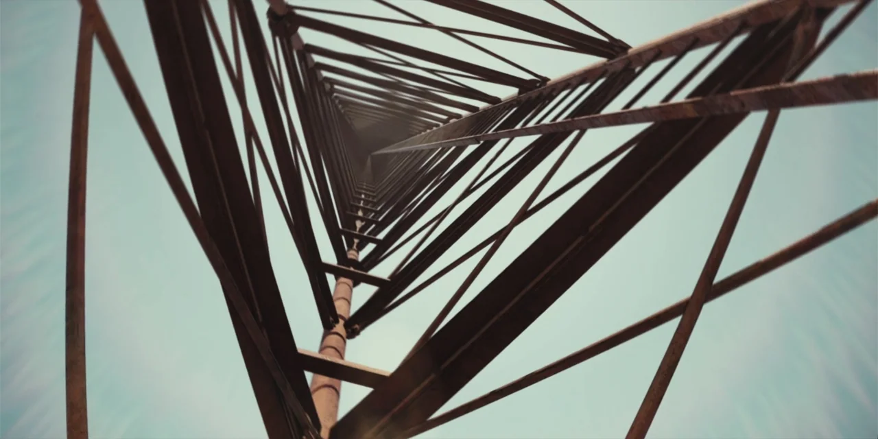 Fall (2022) movie still: establishing — A vertical metal radio tower framework reaches toward a bright blue sky. The camera looks directly upward…