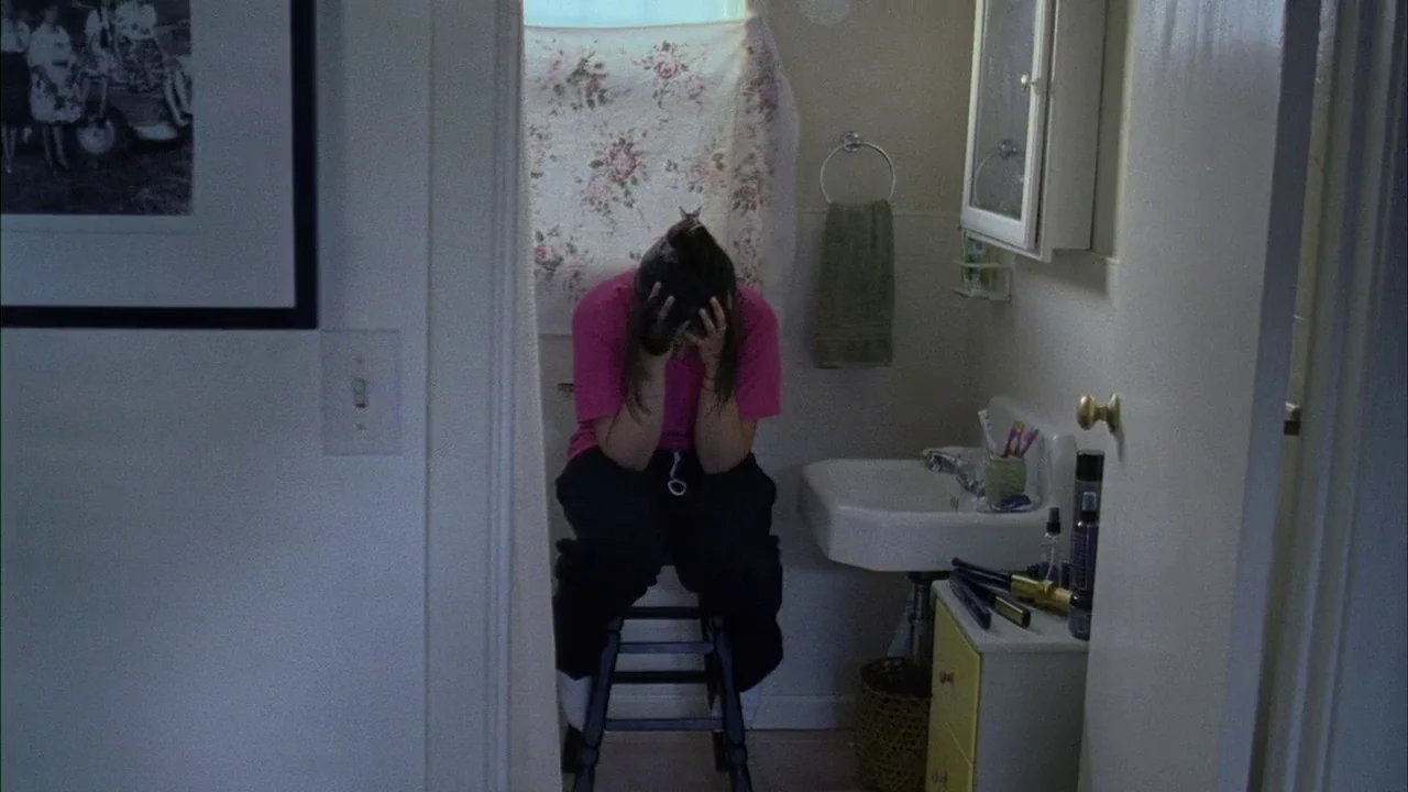 Fruitvale Station (2013) movie still: medium — A small residential bathroom features a pedestal sink and a floral patterned curtain. A young woman…