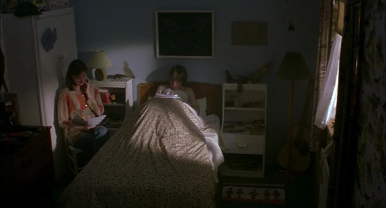 A Room For Romeo Brass (1999) movie still: medium — A cluttered child's bedroom with blue walls and a bed covered in a floral quilt. A woman sits on…