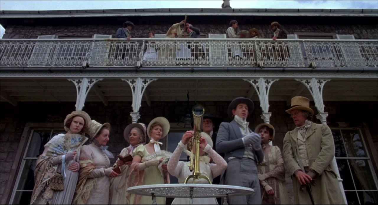 Gothic (1986) movie still: wide — A stone mansion with an ornate wrought iron balcony stands beneath an overcast sky. A group of people dressed in…