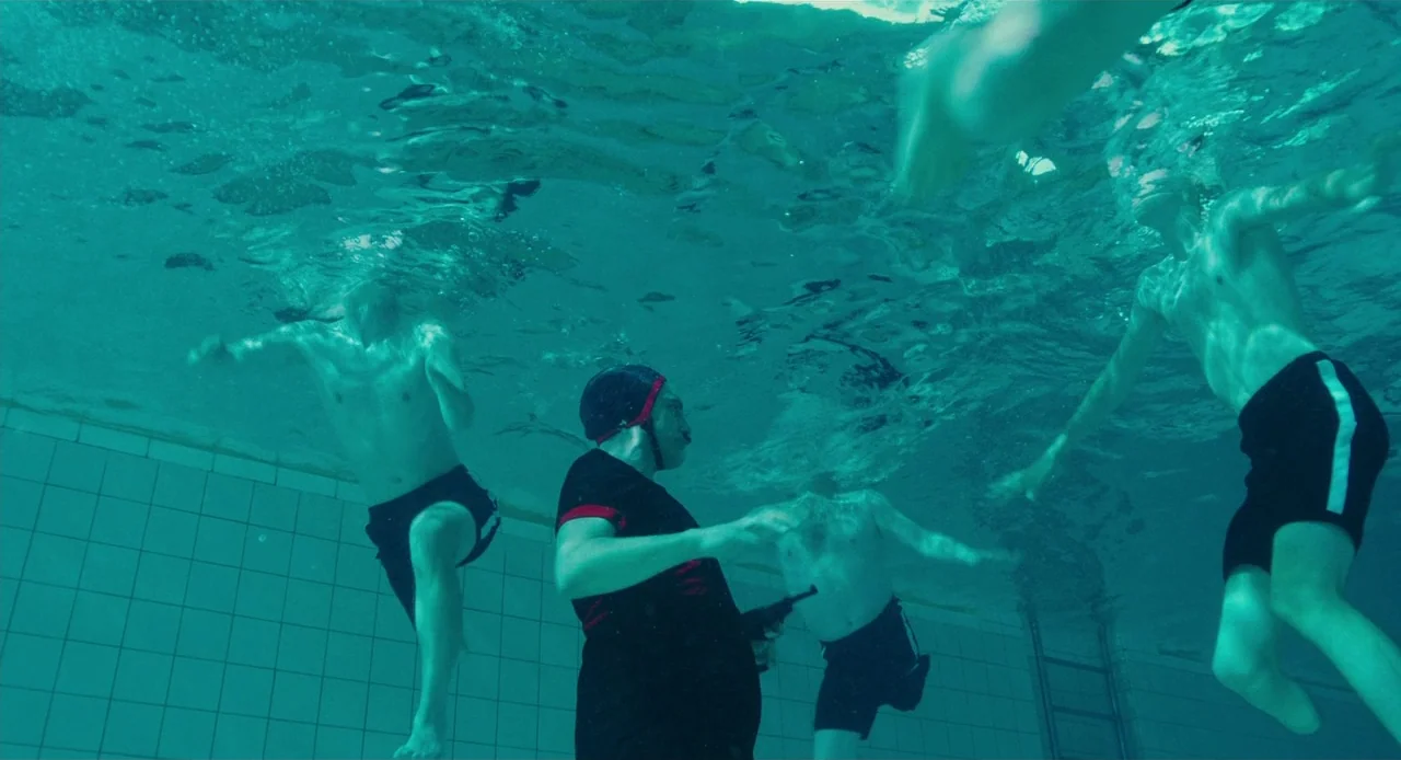 Jojo Rabbit (2019) movie still: wide — A group of people navigate the water inside an indoor facility with white tiled walls. One man holds a black…