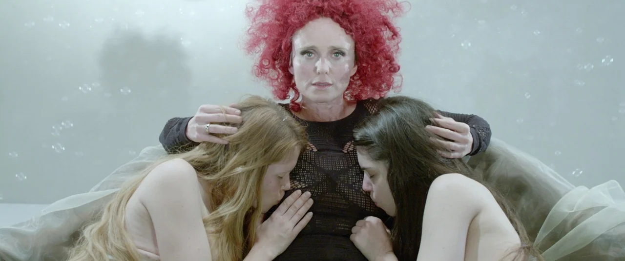 The Lure (2015) movie still: medium — A stark white studio setting features floating translucent soap bubbles in the background. A woman with bright…