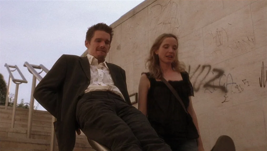 Before Sunset (2004) movie still: medium — A set of outdoor stone stairs features a beige concrete wall covered in graffiti. A man in a suit and a…