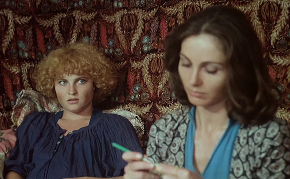 L’une Chante, l’Autre Pas (1977) movie still: medium — Two women sit in front of a heavily patterned, intricately woven antique wall tapestry. One…